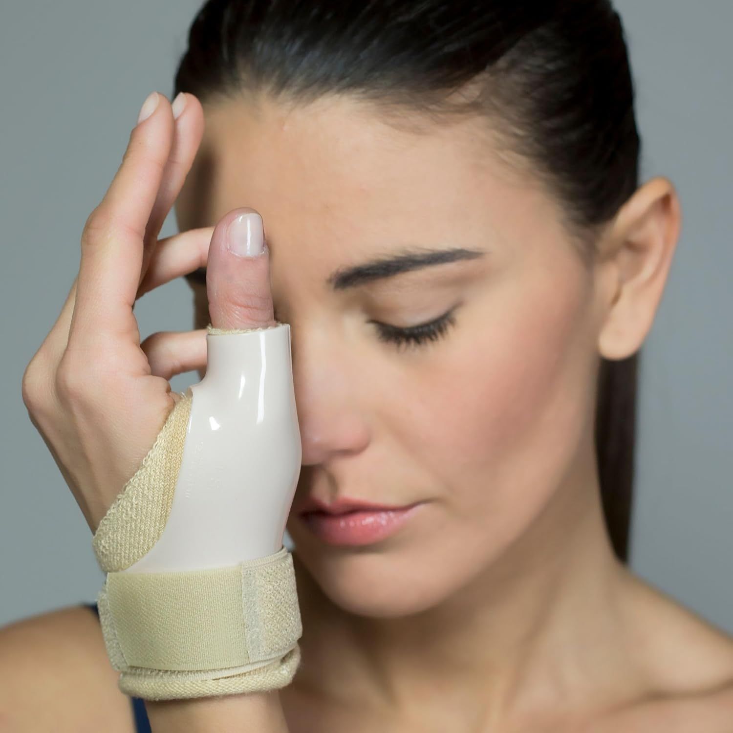 Un tutore bianco per il pollice con chiusure in velcro, fissato al polso e al pollice di una donna.