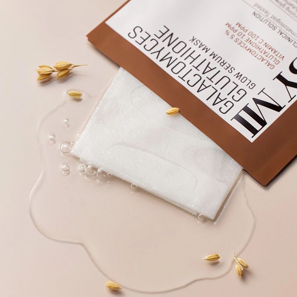 Maschera SOME BY MI con confezione aperta. Maschera bianca su superficie bagnata con chicchi. Testo: Galactomyces Glutathione Glow Serum Mask.