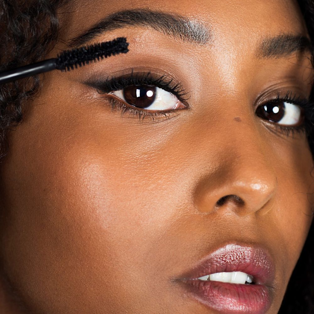 Primo piano di una donna che applica il mascara. Spazzola sull'occhio. Pelle scura, capelli scuri.