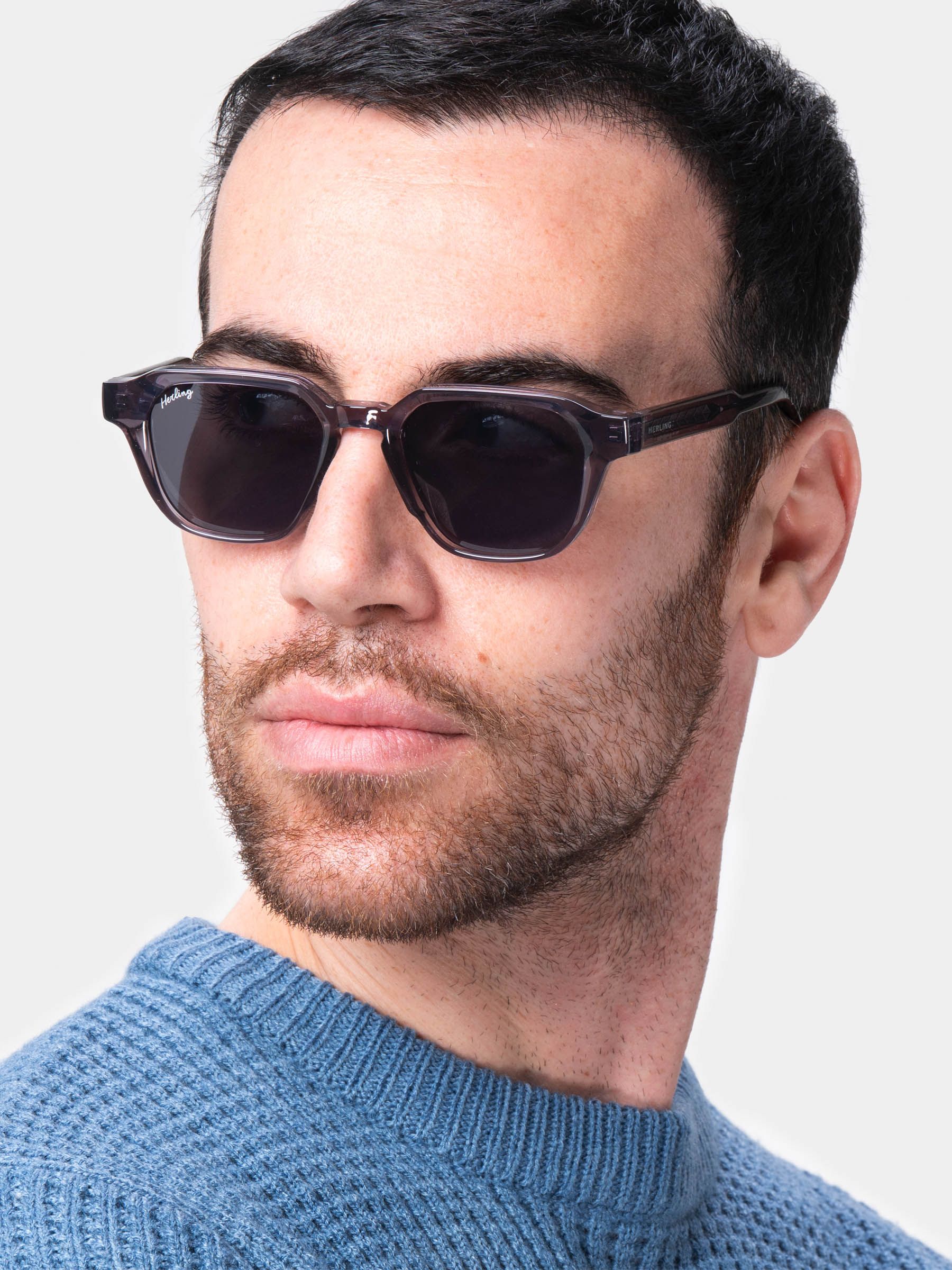 Uomo con occhiali da sole grigi. Il marchio Herling è visibile sull'asta.