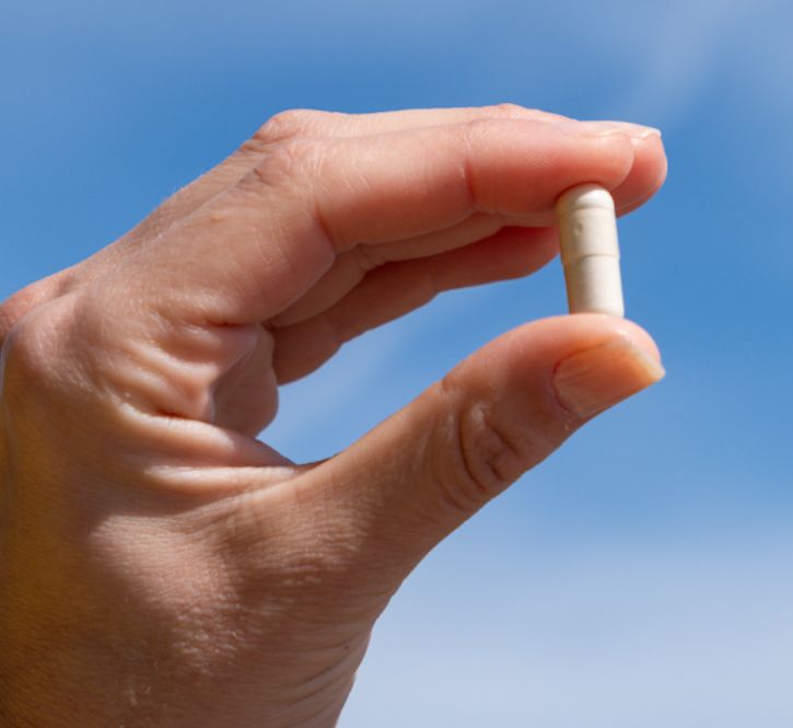 Mano che tiene una capsula Aavalabs Multivitamin davanti al cielo blu.