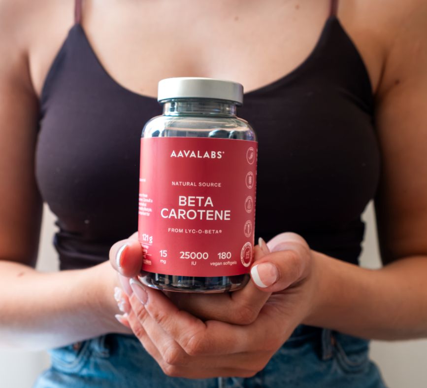 Persona che tiene un flacone Aavalabs Beta Carotene. 180 softgel vegani, 25.000 UI.