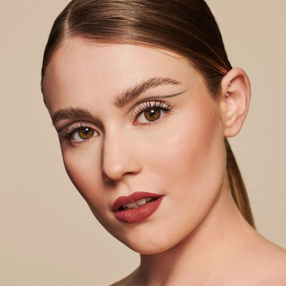 Ritratto di donna truccata. Focus su occhi e labbra. Mascara, eyeliner e rossetto. Sfondo beige.