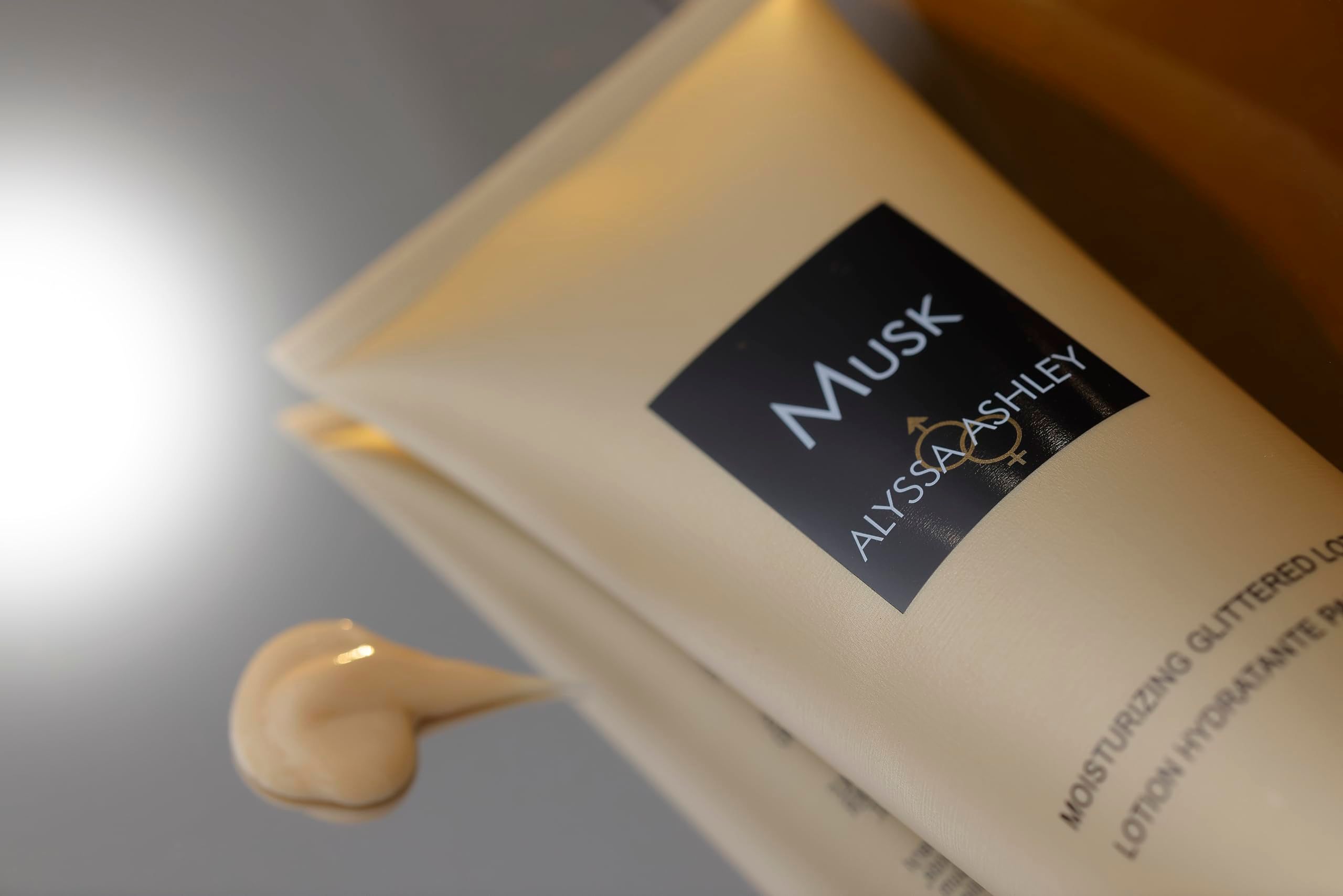 Tubo beige con etichetta nera. Scritta "Musk" e "Alyssa Ashley". Accanto, una goccia di lozione.