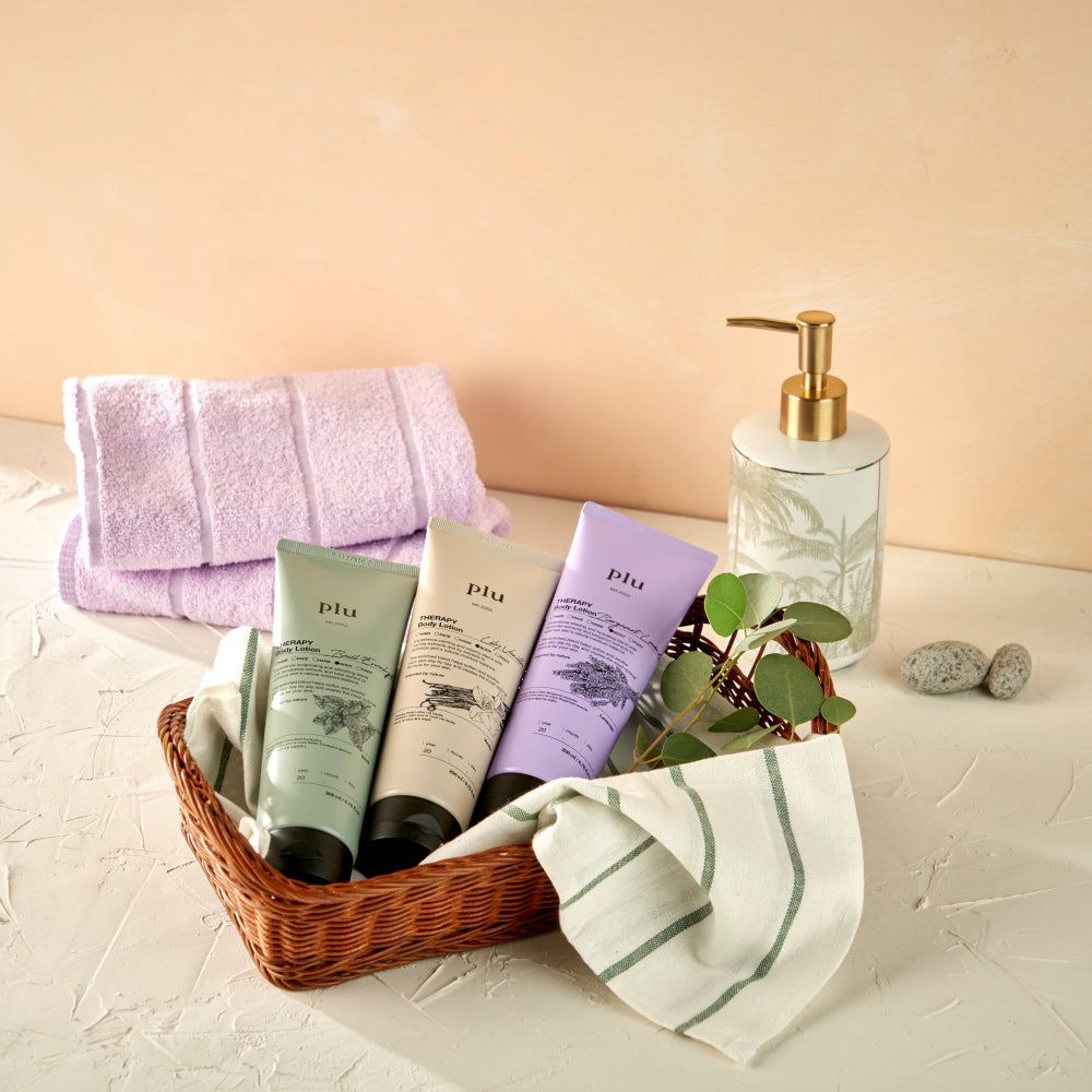 Cesto con tre tubi 'plu AROMA Body Lotion' di colori diversi, asciugamani e dispenser di sapone.