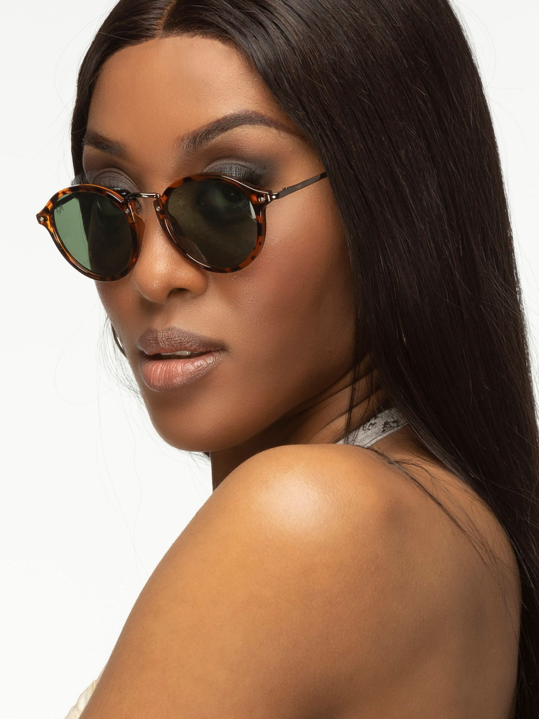 Donna con occhiali da sole Twig. Forma rotonda, montatura marrone tartarugato, lenti verdi. Logo Twig.