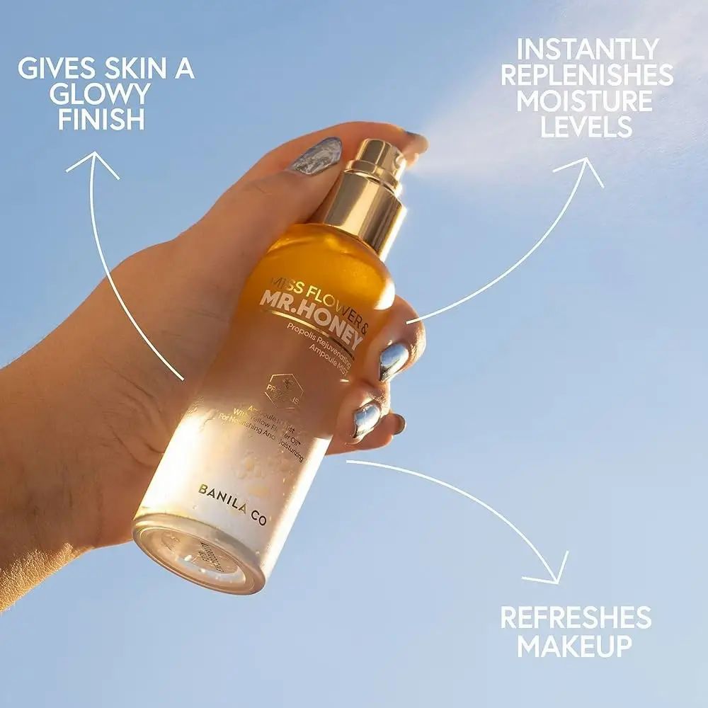 Mano che spruzza spray viso. Erogatore dorato, flacone trasparente con liquido giallo. Scritta: Miss Flower & Mr. Honey.