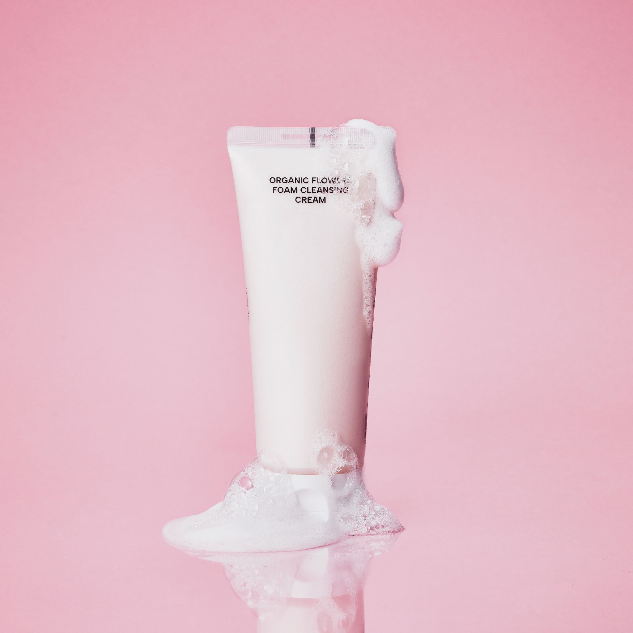 Tubo con schiuma, scritta "ORGANIC FLOWERS FOAM CLEANSING CREAM". Sfondo rosa.