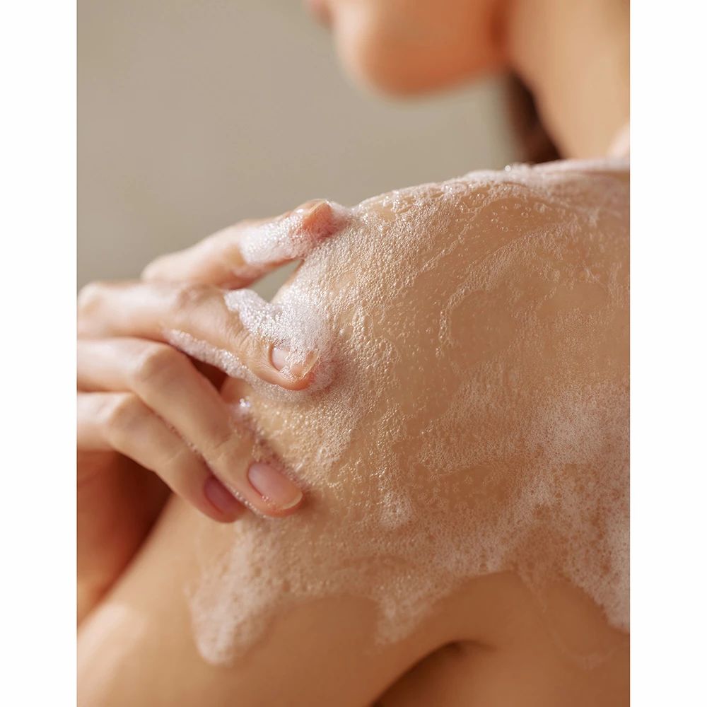 Mano che lava la spalla con il detergente corpo schiumoso SOMEBYMI AHA BHA PHA 30 giorni Miracle Acne Clear.