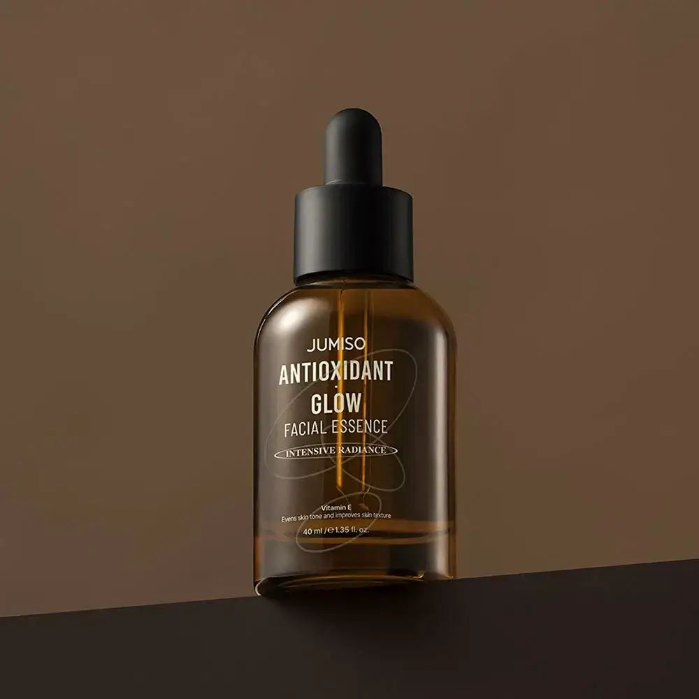 Flacone di vetro marrone con tappo nero e pipetta. Scritta: JUMISO ANTIOXIDANT GLOW FACIAL ESSENCE.