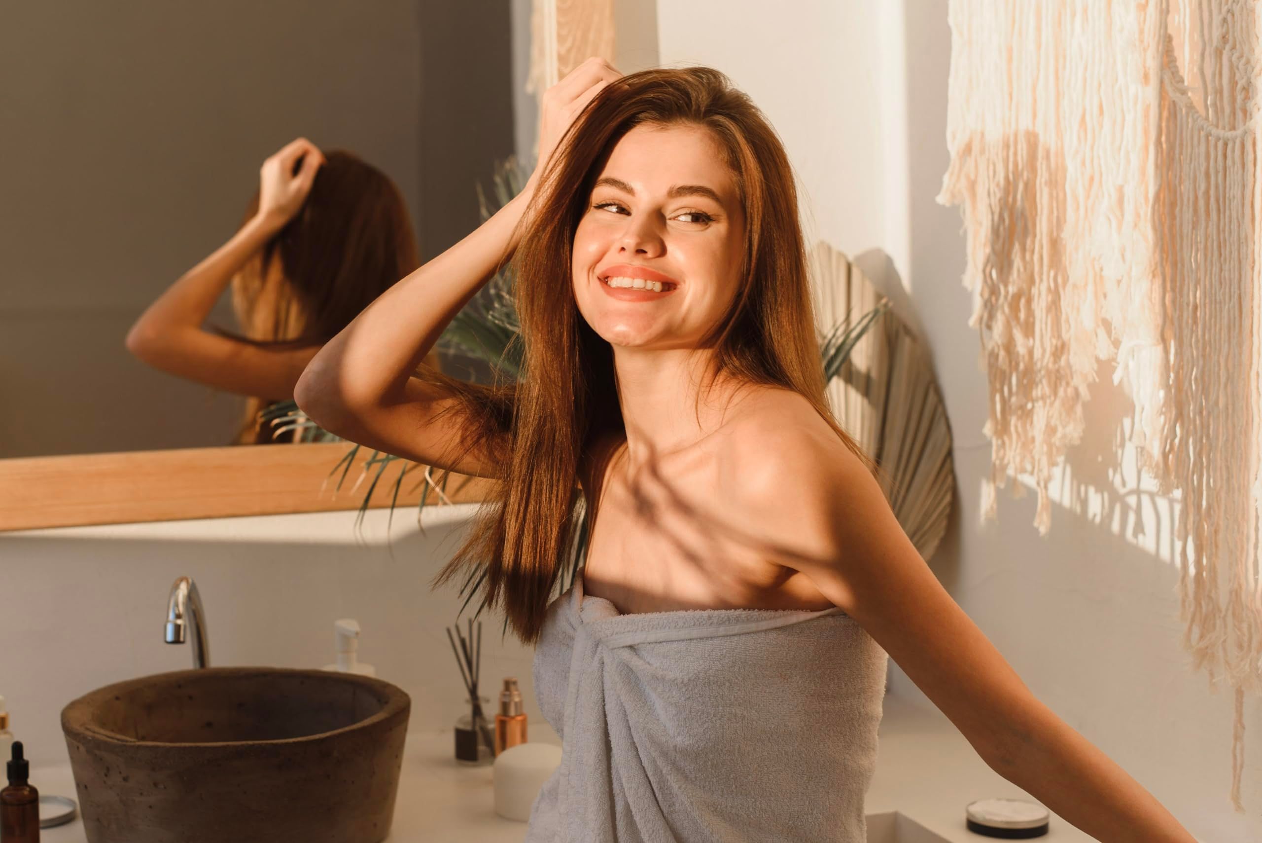 Donna in bagno, avvolta in un asciugamano. Specchio e lavandino sullo sfondo.