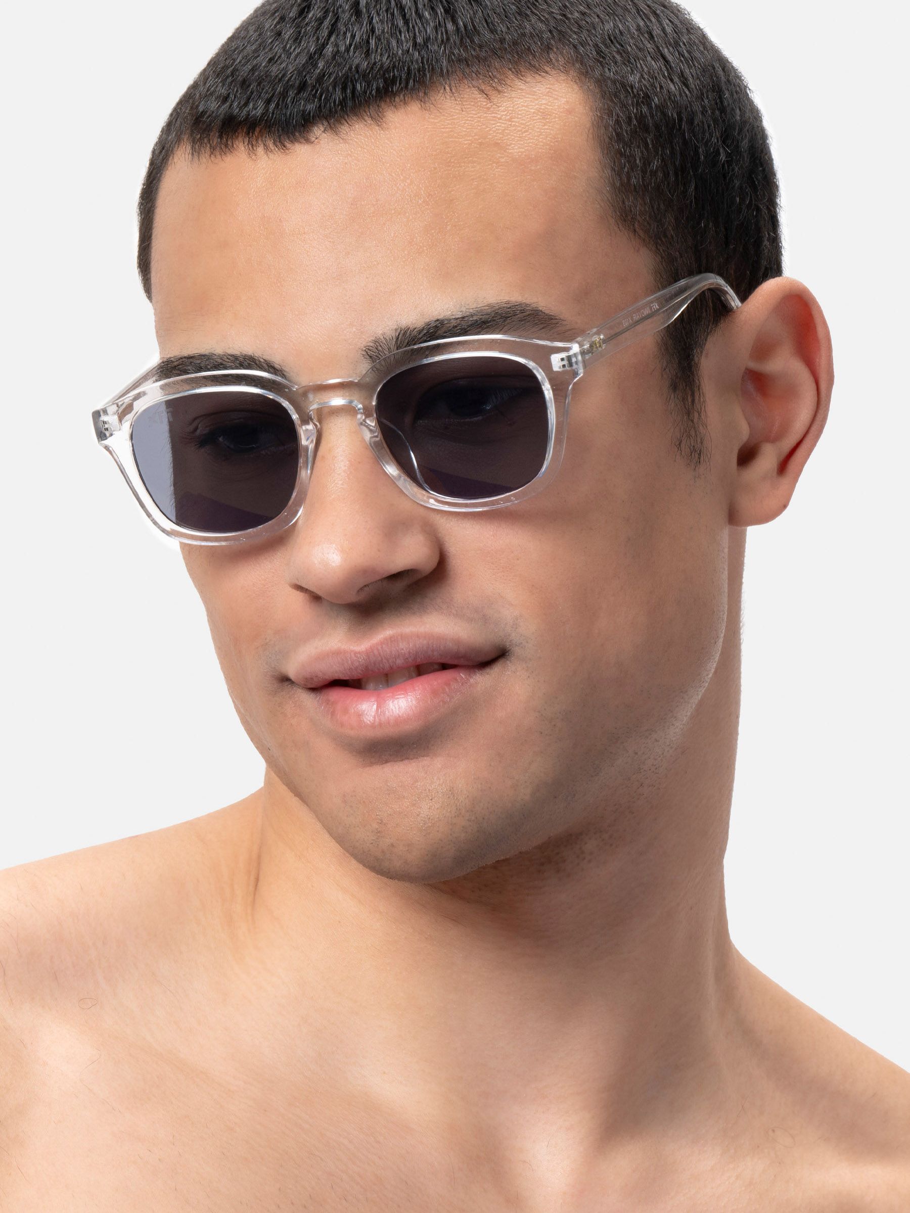 Uomo con occhiali da sole con montatura trasparente e lenti scure. Forma squadrata.