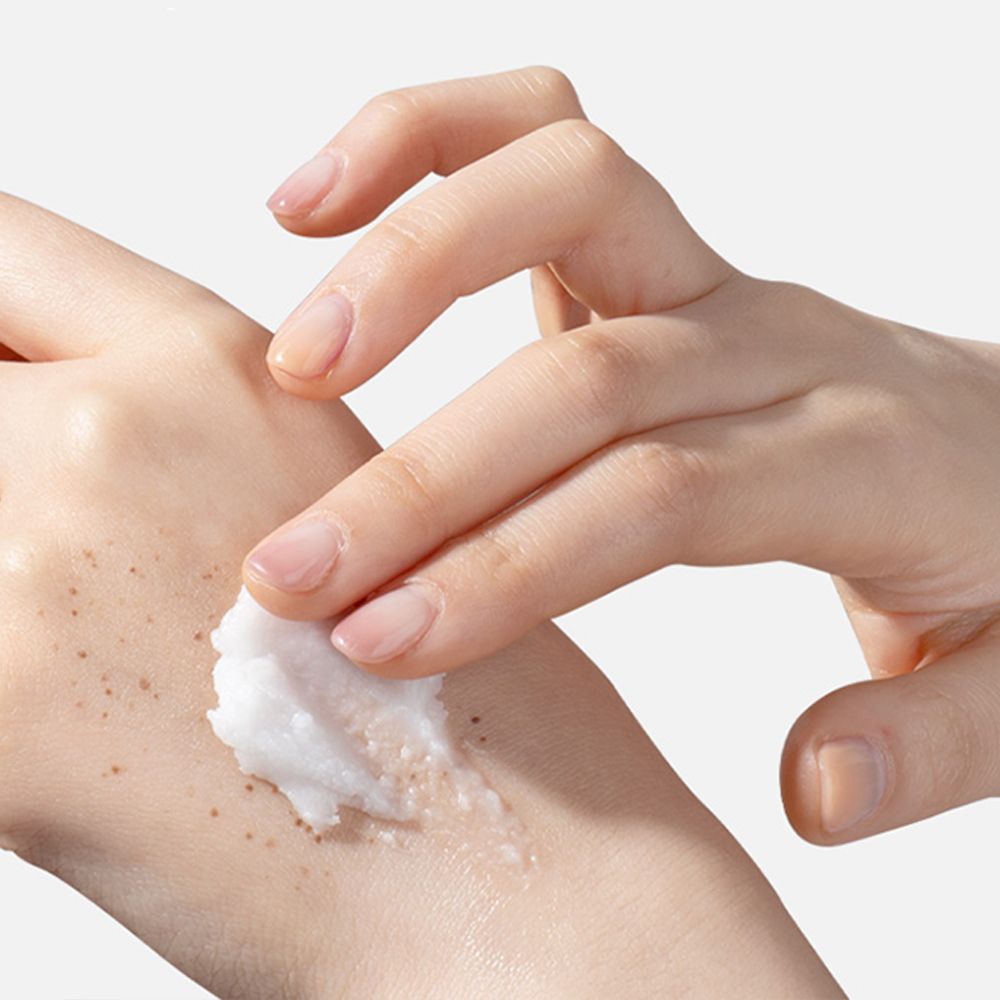 Mano che applica TIRTIR Hydro Boost Enzyme Cleansing Balm sull'altra mano con lentiggini.