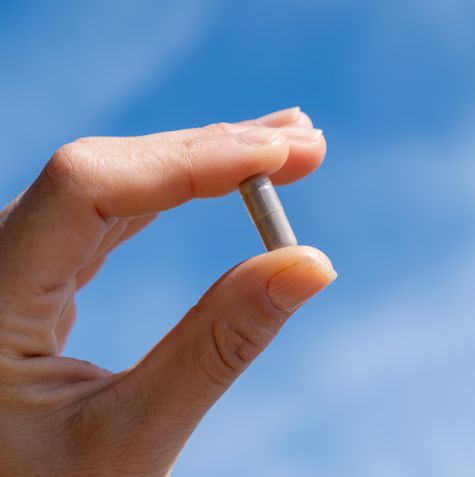 Mano che tiene una singola capsula Aavalabs Ferro Bisglicinato davanti al cielo blu.