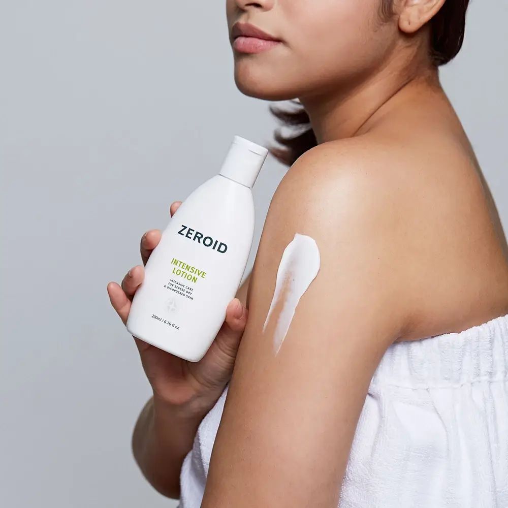Persona che tiene in mano un flacone di ZEROID Intensive Lotion. Crema applicata sul braccio. Asciugamano bianco.