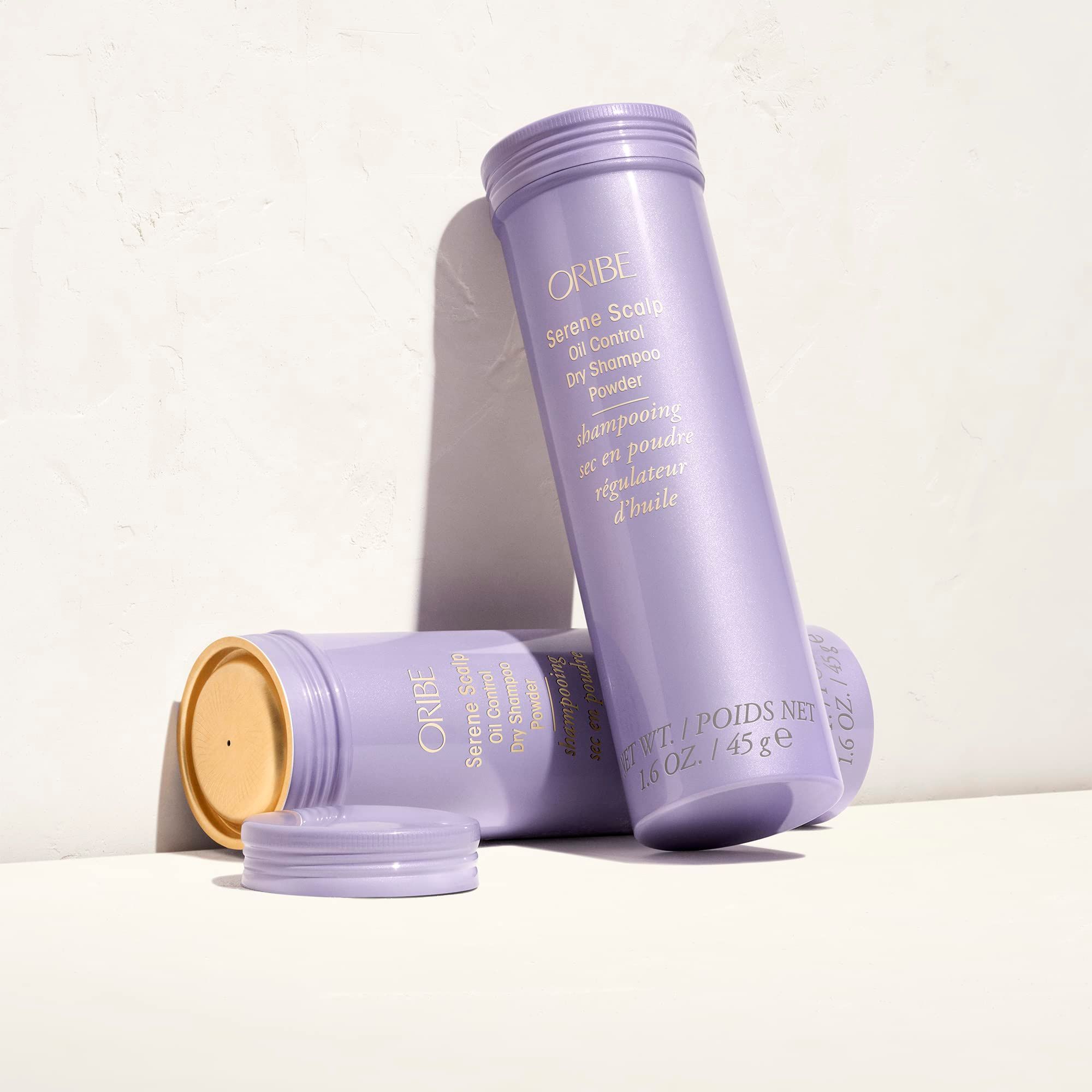 Due flaconi Oribe Serene Scalp Dry Shampoo in polvere. Viola chiaro. Coperchi accanto. Su sfondo chiaro.