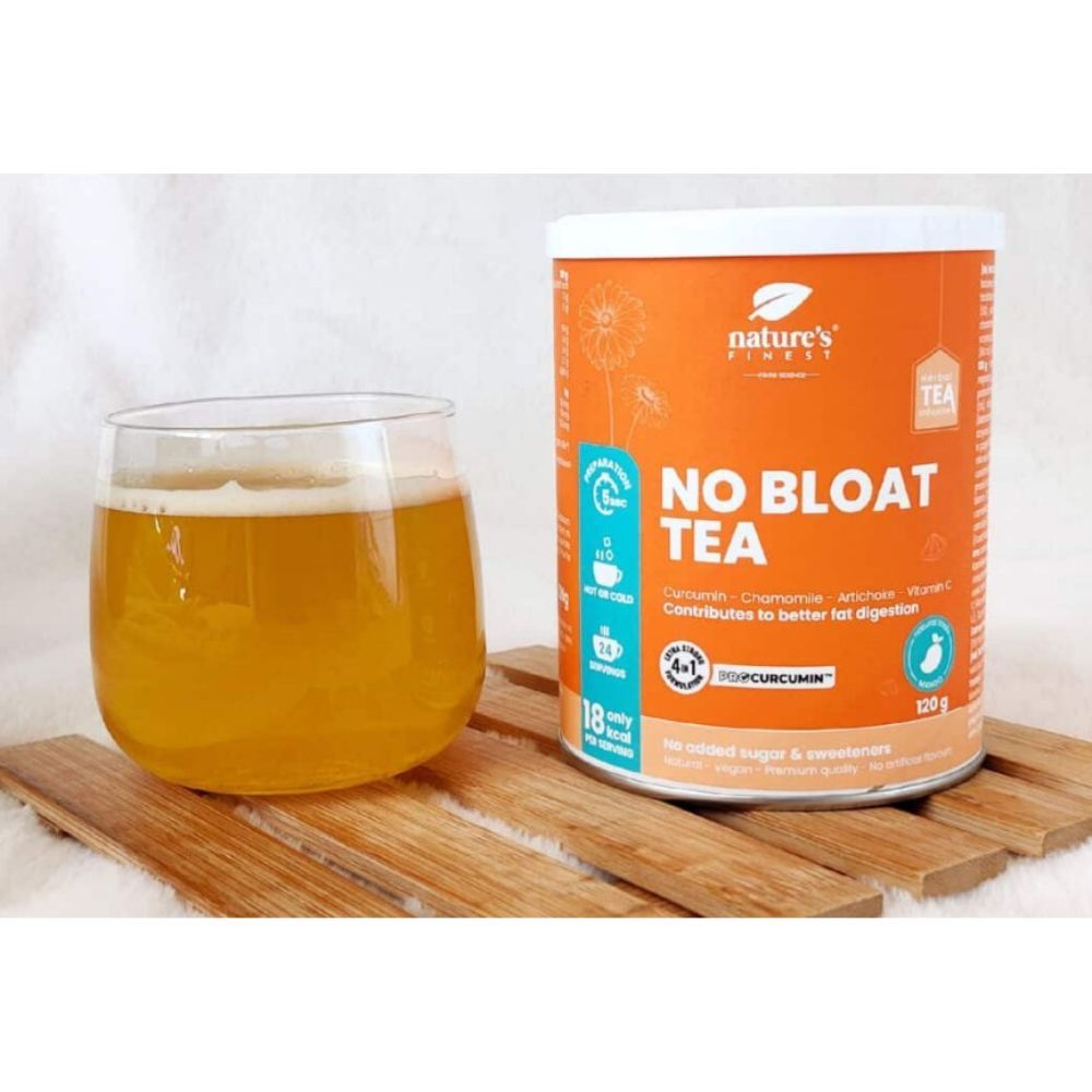 Bicchiere di tè accanto al barattolo "Nature's Finest No Bloat Tea". Tè dorato. Barattolo su tavola di legno. Informazioni sul prodotto visibili.