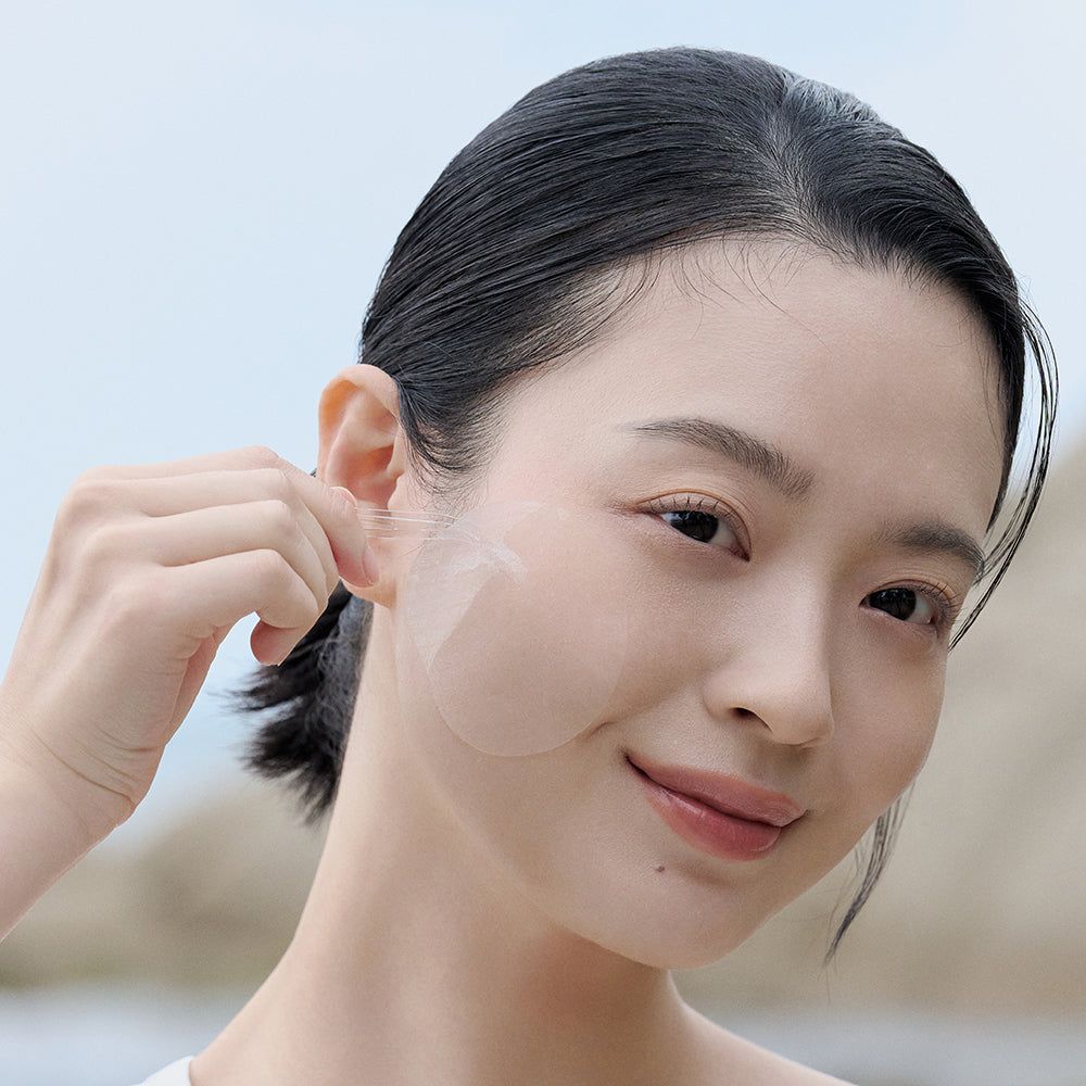 Donna applica un pad trasparente sulla guancia. Pad rotondo e trasparente. Sfondo: natura.