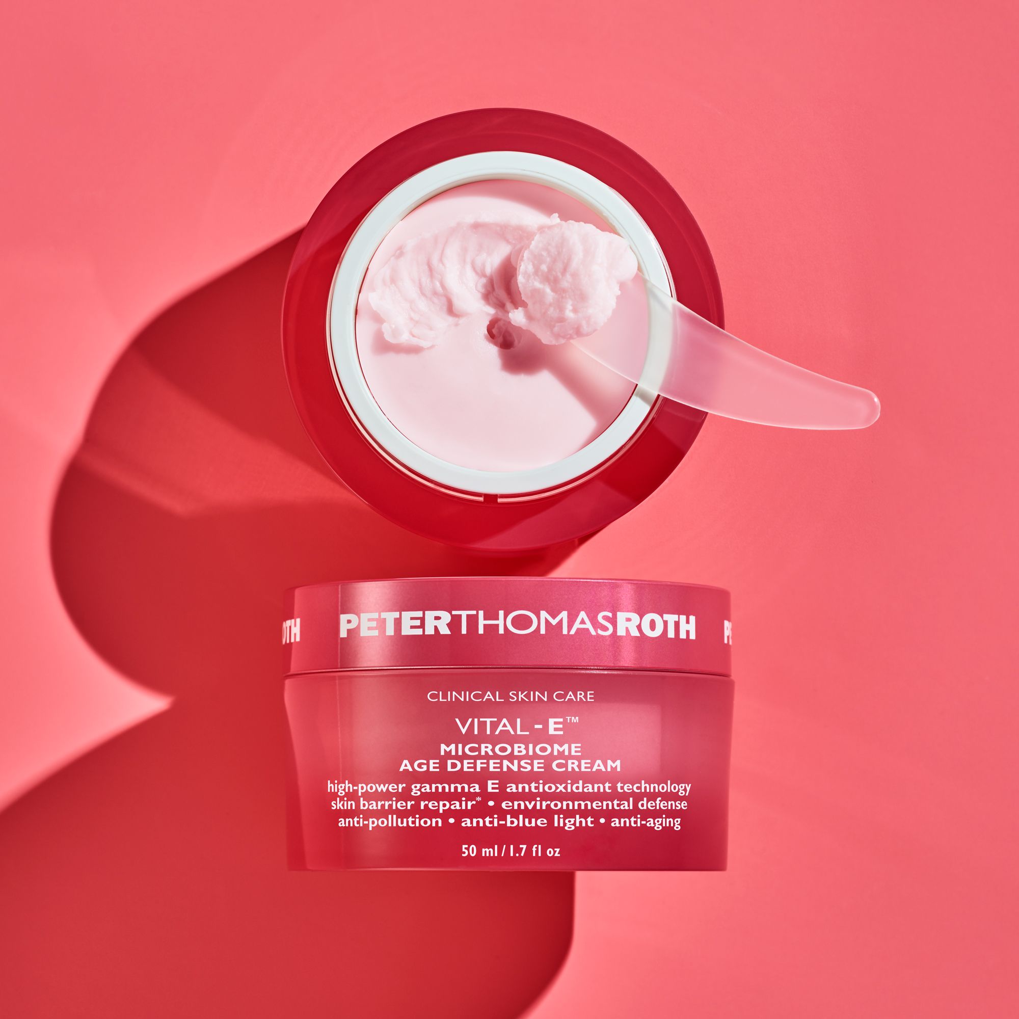 Vaso di crema rosa aperto con crema e spatola. Scritta: Peter Thomas Roth, Vital-E Microbiome Age Defense Cream.
