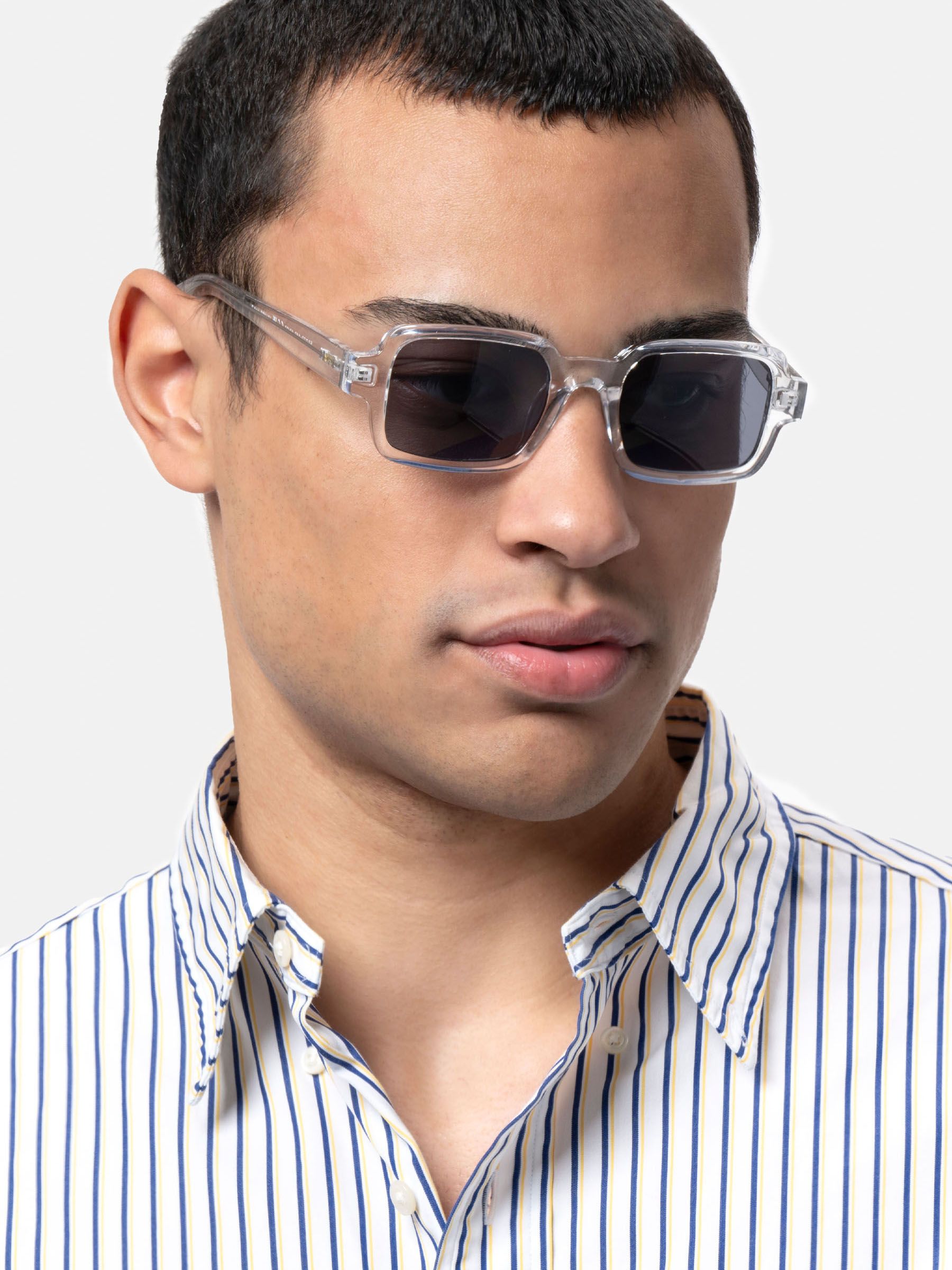 Uomo con occhiali da sole rettangolari con montatura trasparente e lenti scure. Camicia a righe. Primo piano.