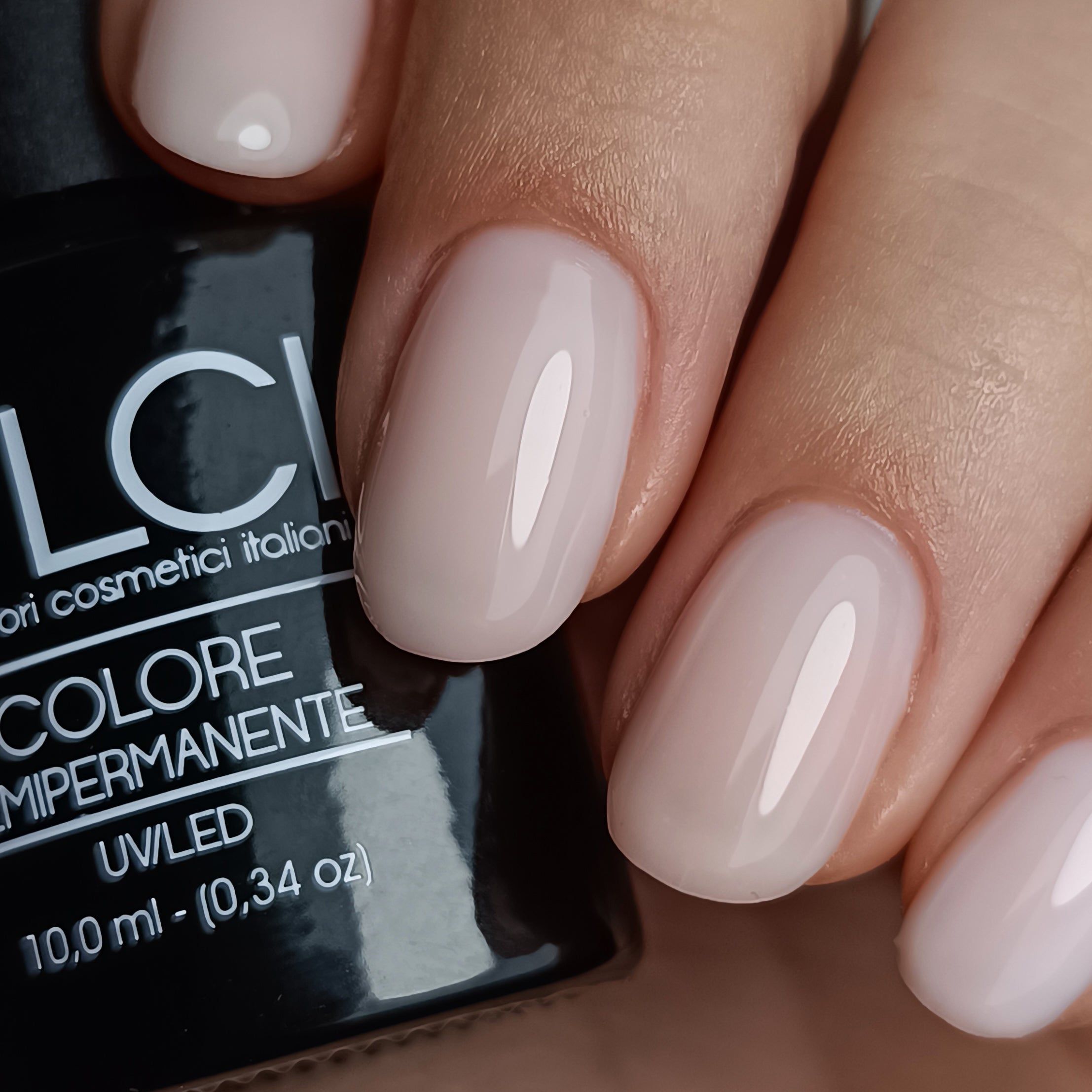 Mano con unghie smaltate. Unghie ovali, smalto rosa chiaro. Flacone con nome del prodotto sullo sfondo.