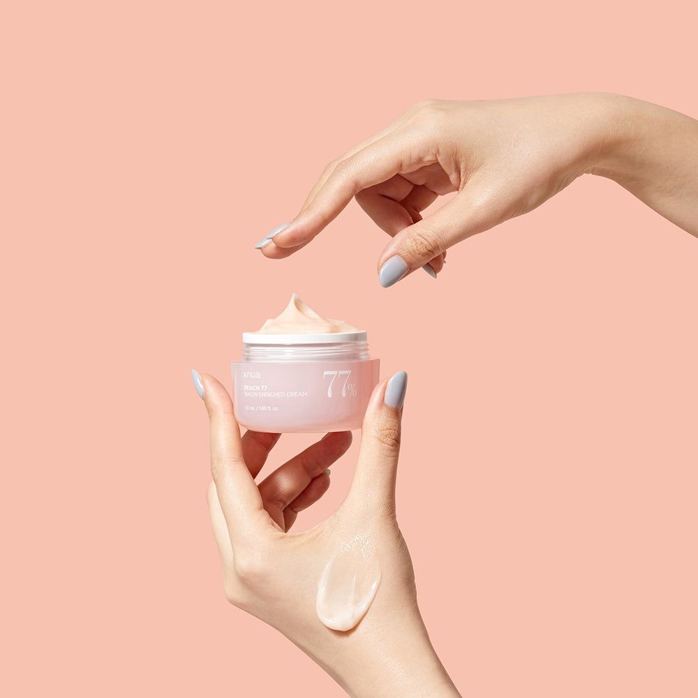 Mani che tengono e toccano un vasetto di crema rosa. Scritta: Anua, PEACH 77, Niacin Enriched Cream, 77%.
