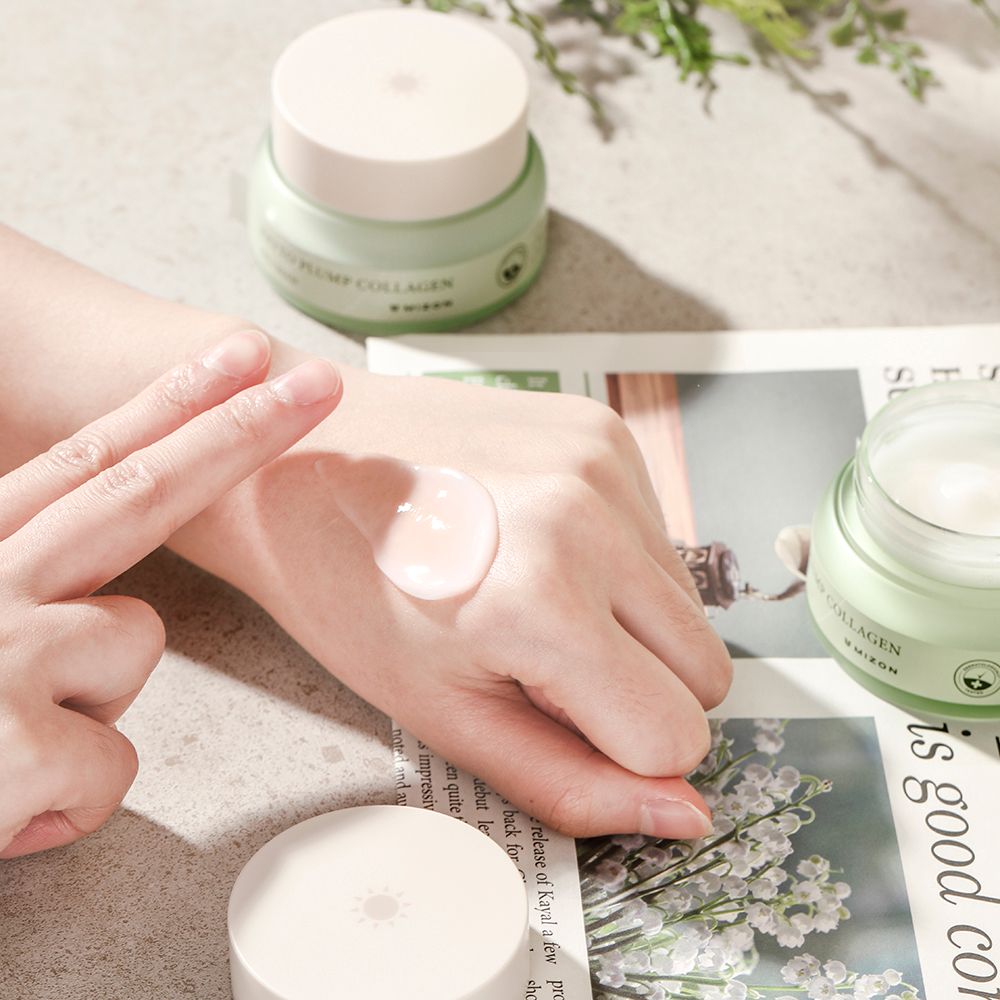 Mano con crema sulla pelle. Vasetto di crema sullo sfondo. Scritta: Phyto Plump Collagen. Marchio: Mizon.