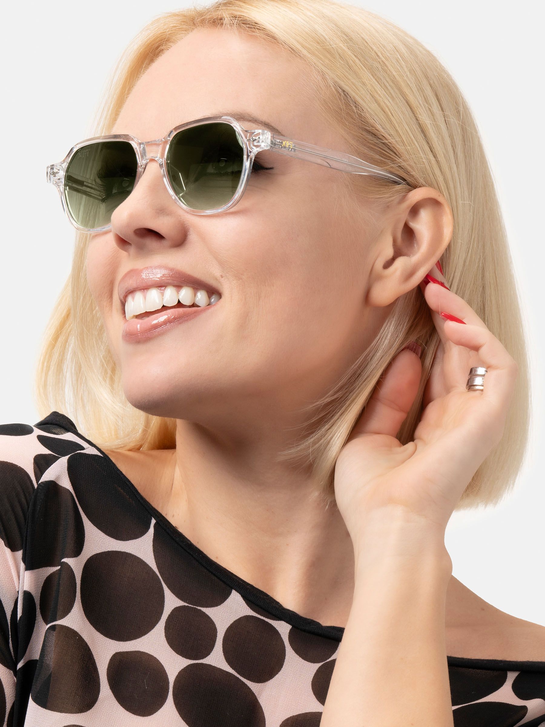 Primo piano di una donna con occhiali trasparenti e lenti verdi. Logo XFT visibile. Forma esagonale.