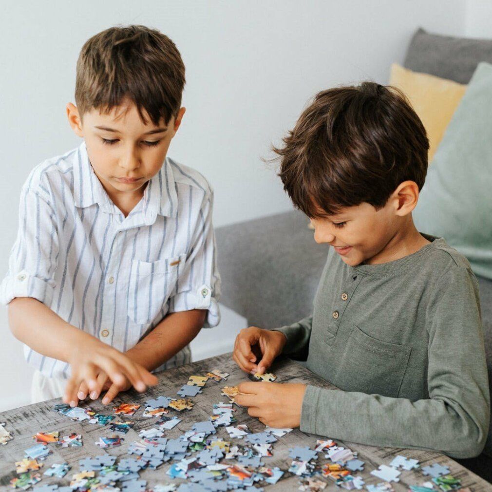 Due bambini fanno un puzzle sul tavolo. Molti pezzi sparsi. Concentrazione sull'assemblaggio.