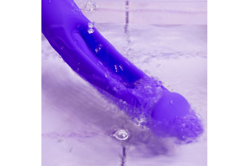 Vibratore viola nell'acqua. L'acqua schizza sul vibratore. Il vibratore è parzialmente immerso.