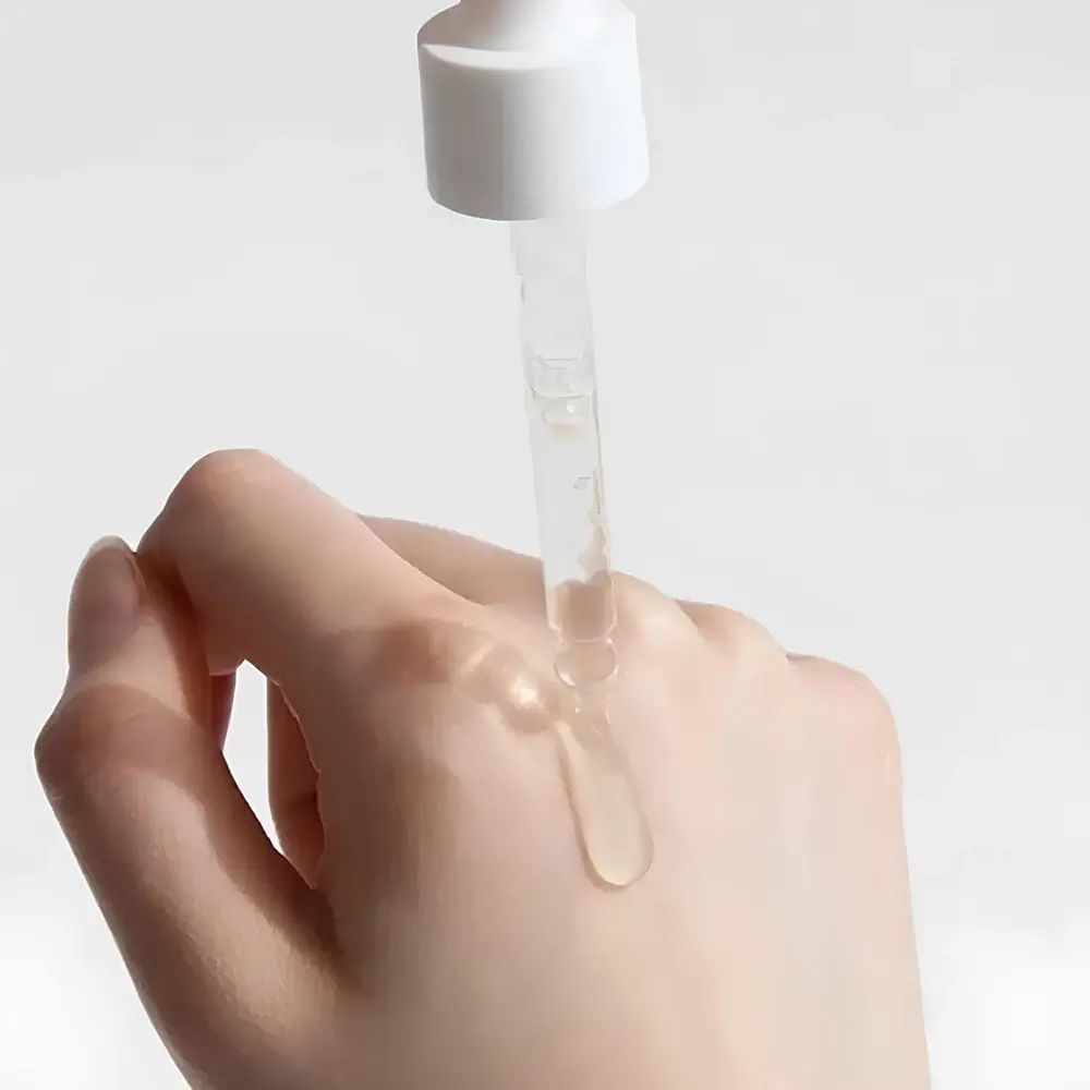 Mano con gocce di essenza. Pipetta che eroga liquido sulla pelle. Liquido trasparente.