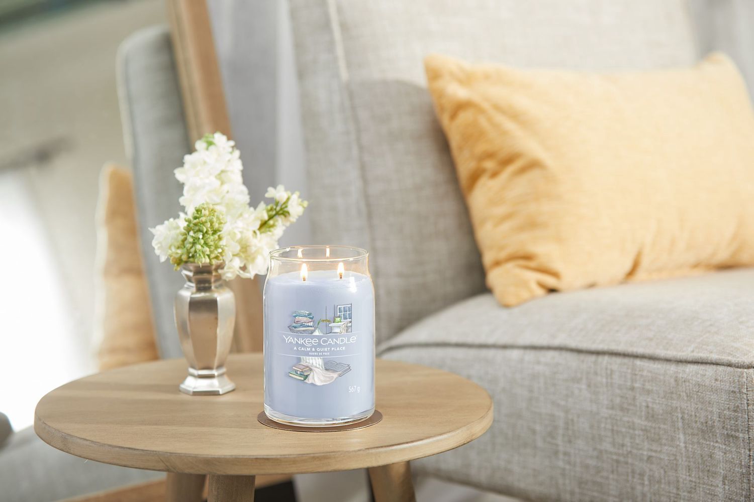 Candela profumata Yankee Candle su un tavolo. Cera blu in barattolo di vetro. Scritta: A Calm & Quiet Place. Accanto a vaso con fiori.
