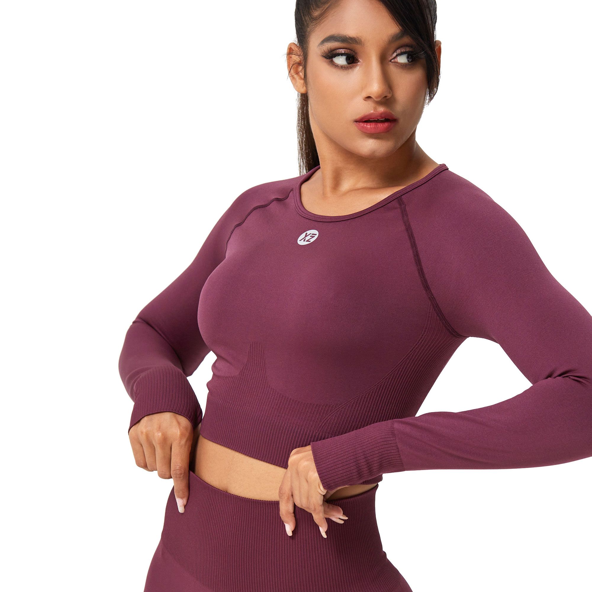 Donna con crop top bordeaux a maniche lunghe, scollo rotondo e piccolo logo sul petto.