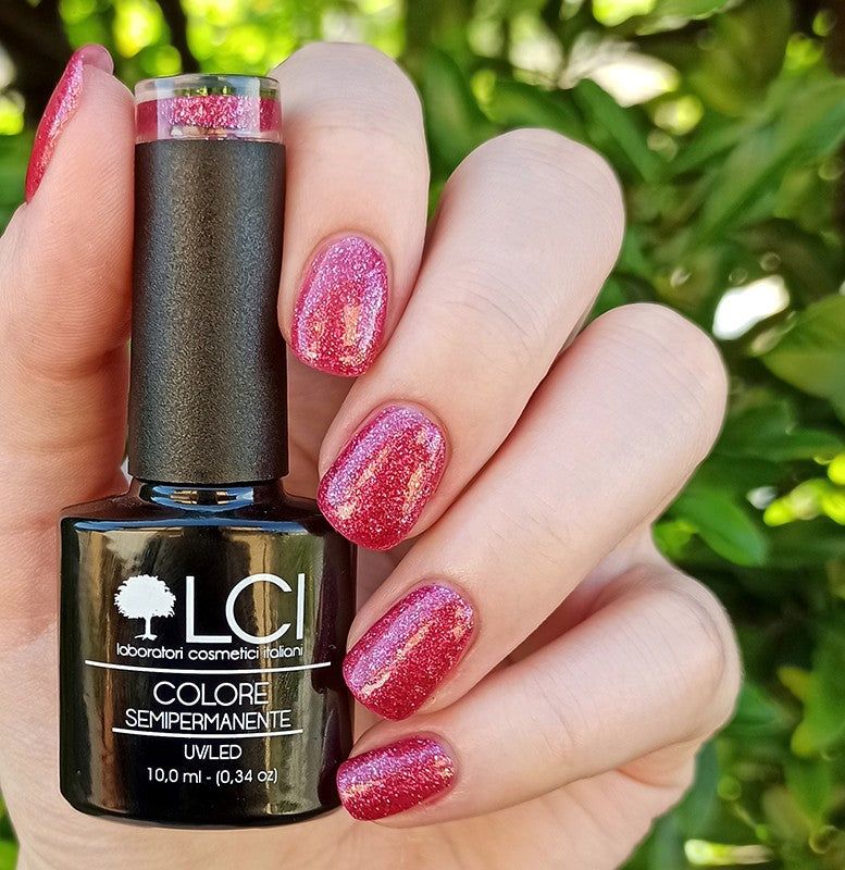 Flacone di smalto e unghie smaltate. Tonalità rosa con glitter. Tappo nero, flacone quadrato con etichetta. Mano.