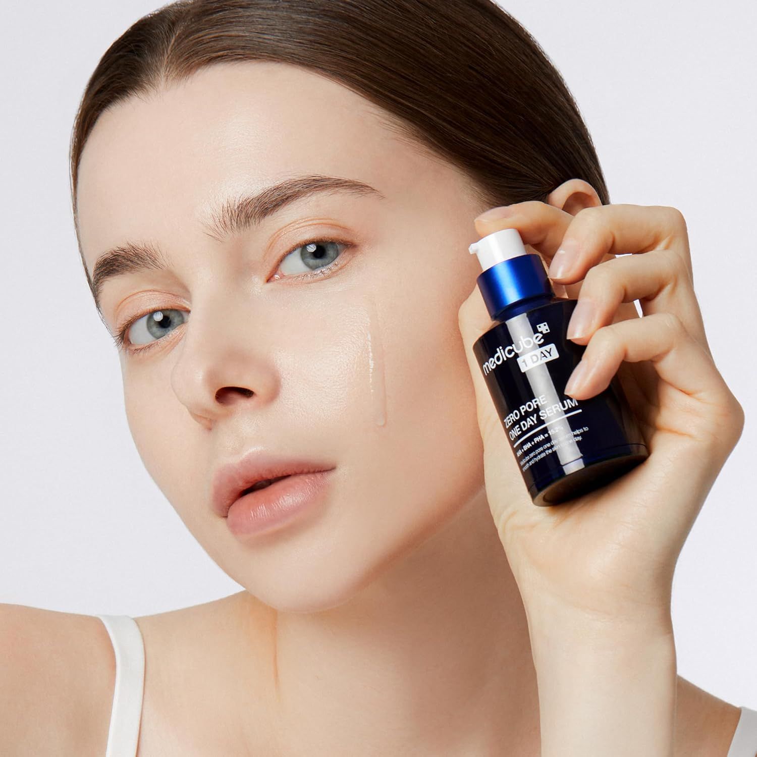 Donna che tiene in mano un flacone di MEDICUBE Zero Pore One Day Serum. Il prodotto viene applicato sulla pelle. Tappo blu.