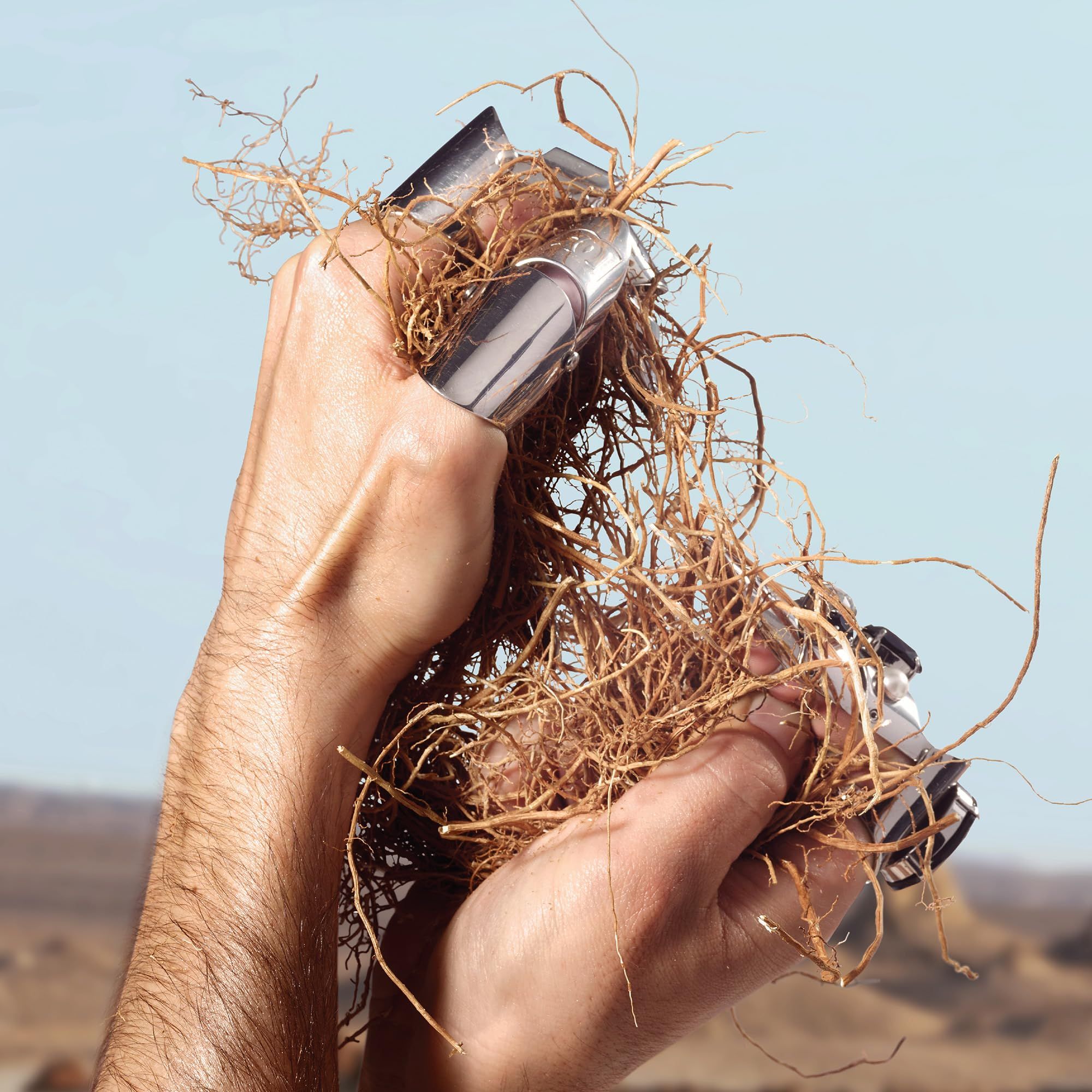 Mani che tengono anelli d'argento e radici. Sfondo: paesaggio desertico.