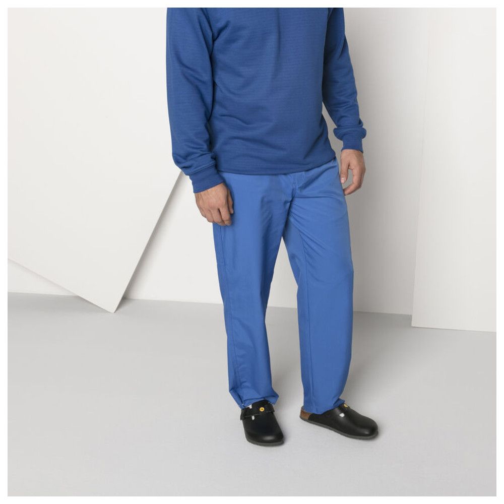 Persona che indossa zoccoli neri. Pantaloni e top blu. Scarpe con logo giallo. Ambiente luminoso.