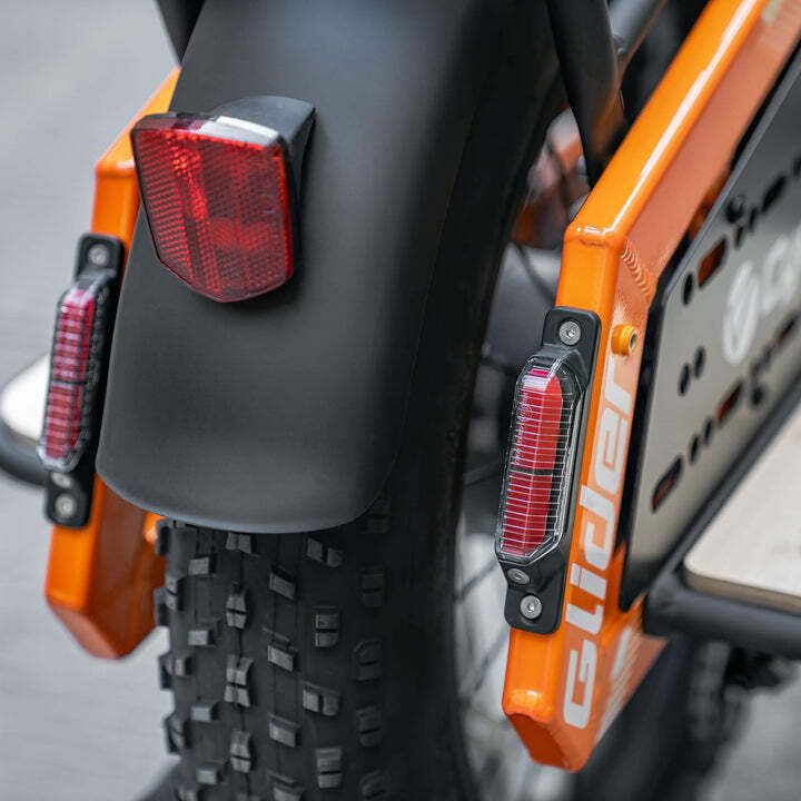 Fanale posteriore e parafango di una bicicletta arancione. Due luci rosse e parafango nero.