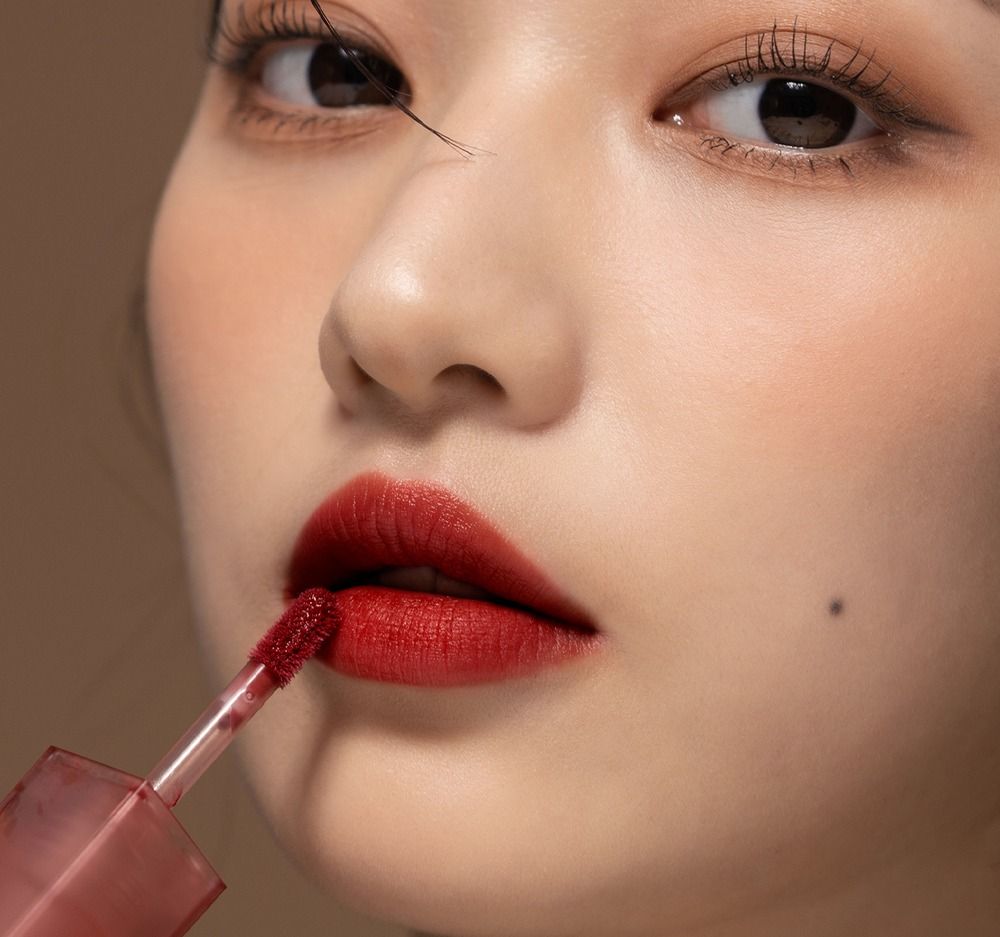 Primo piano di una persona che applica un lucidalabbra rosso scuro. L'applicatore è visibile.