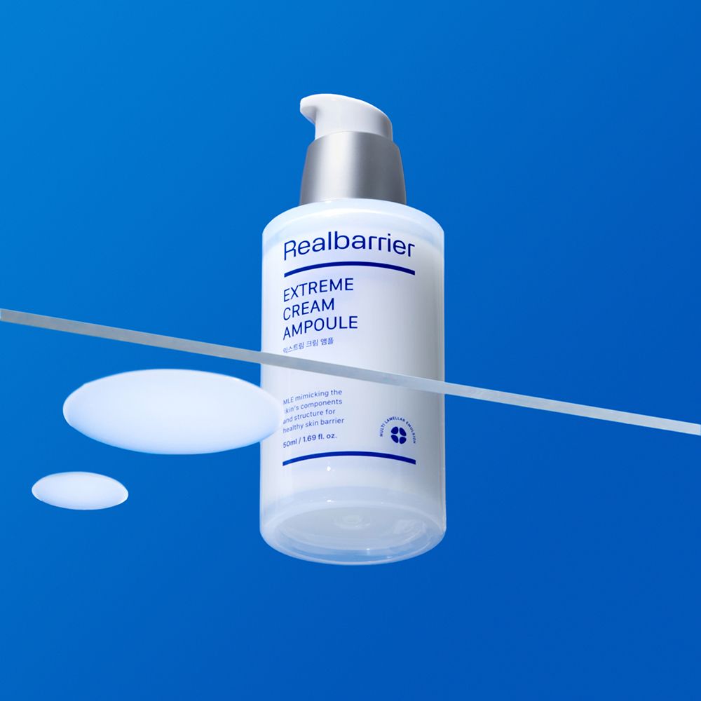 Flacone bianco con erogatore argentato su sfondo blu. Scritta: Realbarrier, Extreme Cream Ampoule.
