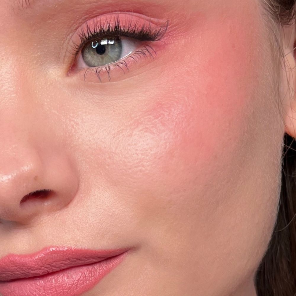 Primo piano di un viso con trucco rosa su occhi, guance e labbra. Occhi verdi.