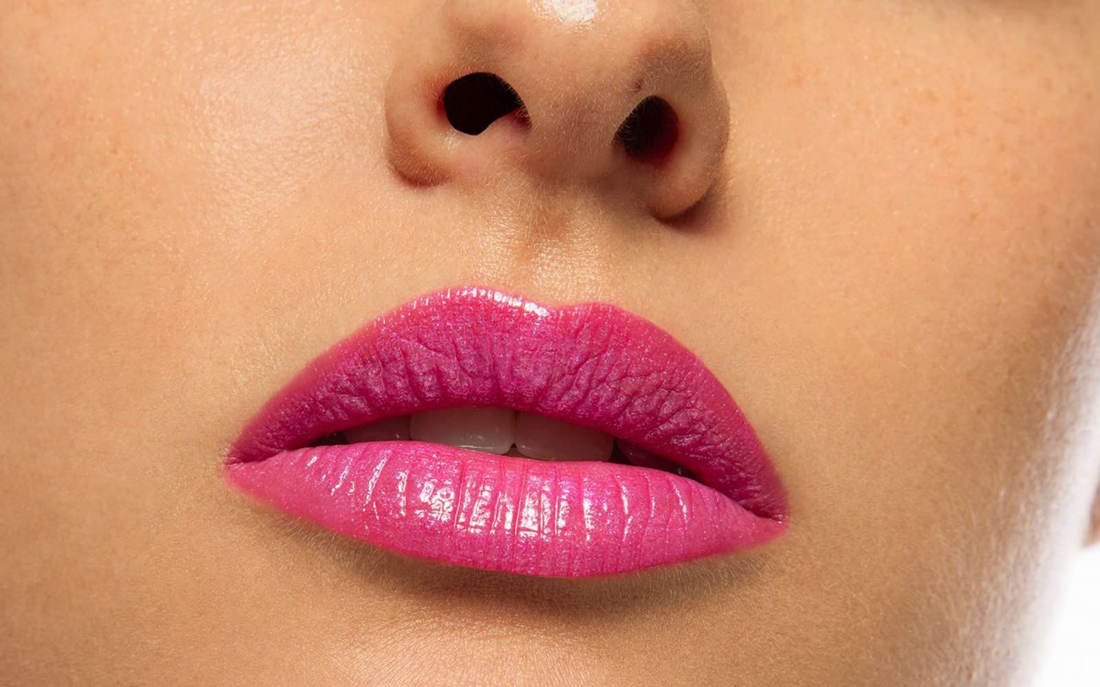 Primo piano di labbra con rossetto rosa. Labbra aperte, denti visibili. Pelle intorno alle labbra.