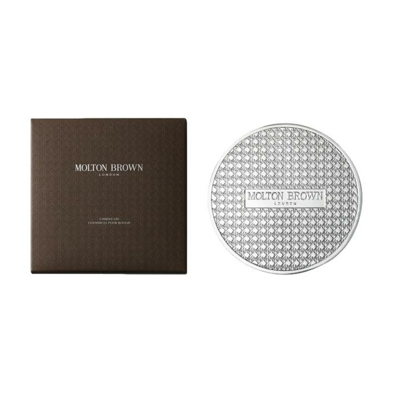 Scatola marrone e coperchio argentato. "Molton Brown London" sulla scatola. Il coperchio è rotondo e ha un motivo.