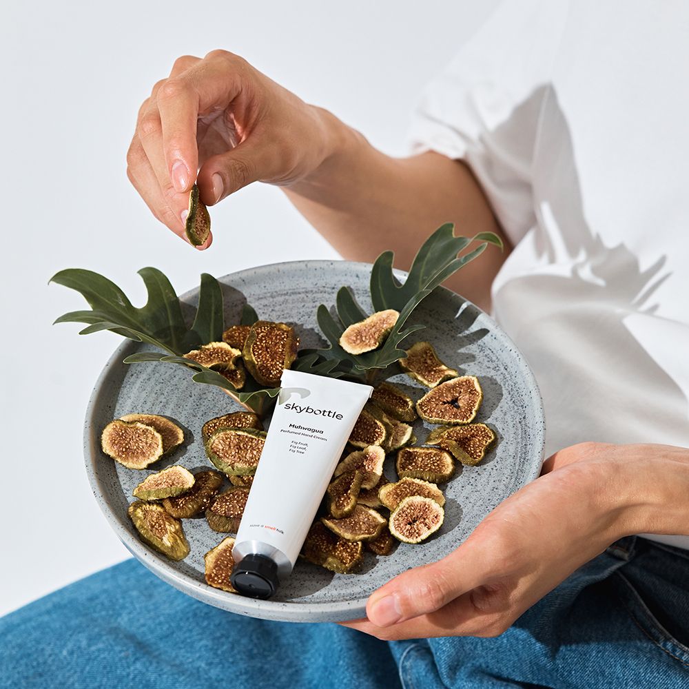 Persona che tiene un fico sopra una ciotola con fichi e foglie. Tubo di crema mani accanto.