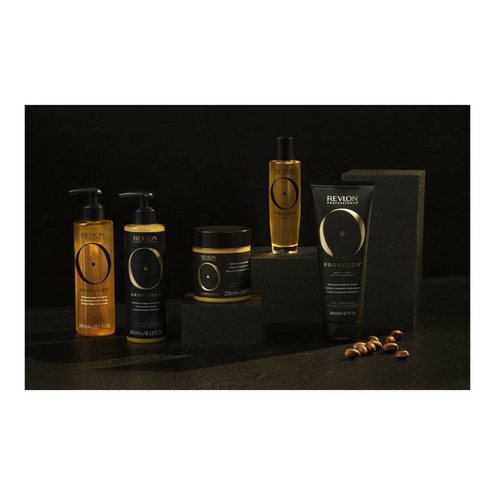 Prodotti Orofluido su sfondo nero. Flaconi, vasi e tubetto in oro e nero. Semi di argan accanto.