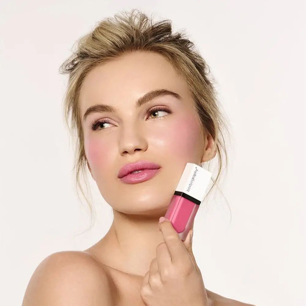 Donna con fard sulle guance. Tiene un tubetto di fard liquido. Marchio BODYOGRAPHY.