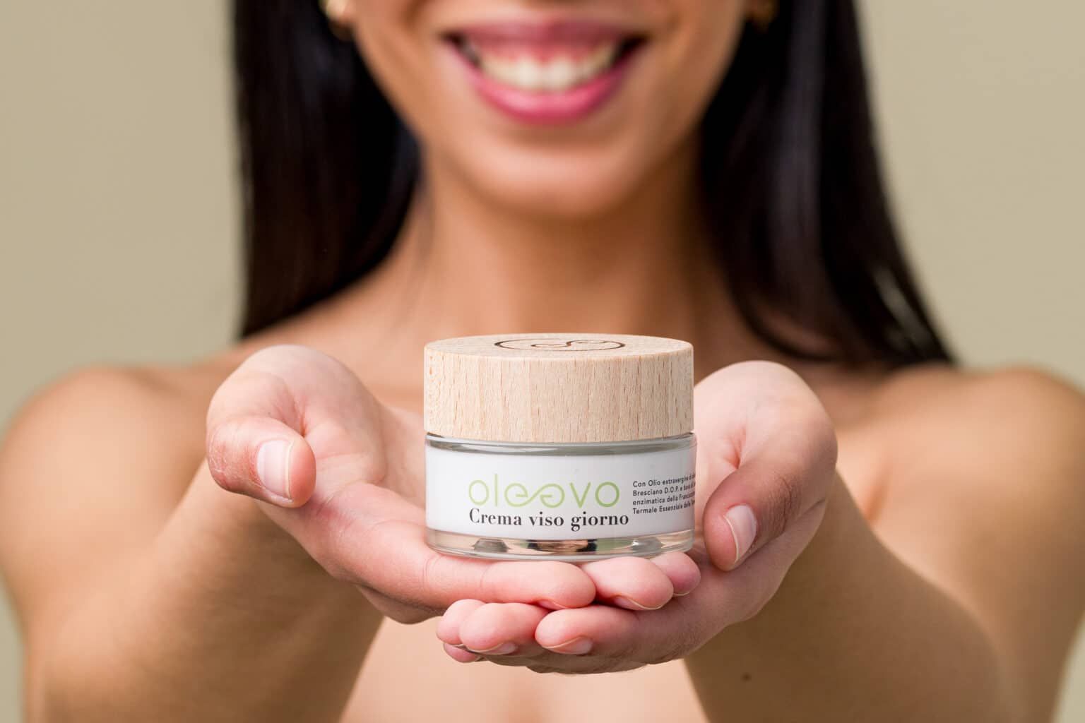 Persona che tiene Oleevo Crema viso giorno tra le mani. Vasetto in vetro con coperchio in legno. Etichetta visibile.