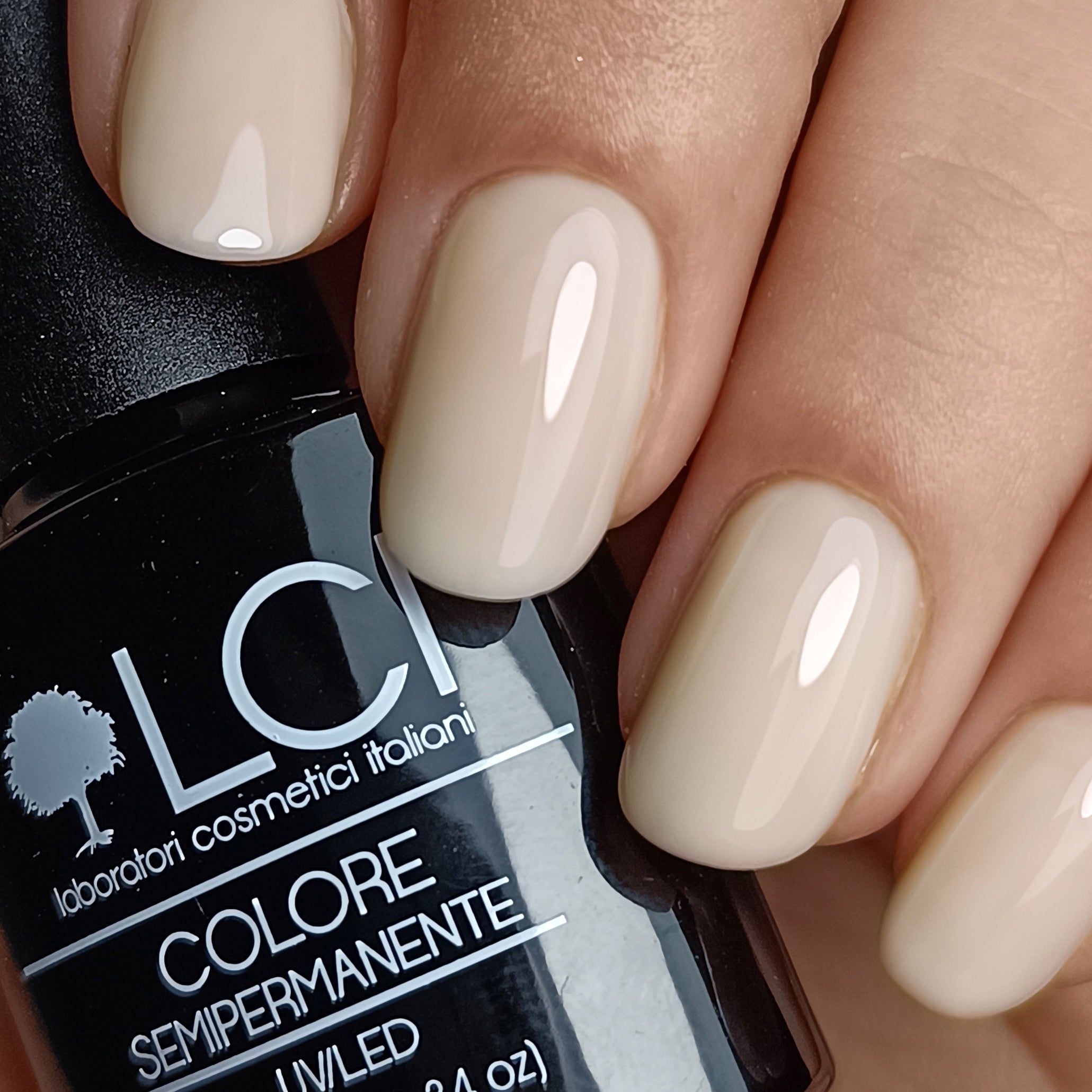 Mano con unghie smaltate beige. Flacone di smalto con scritta: LCI, Colore Semipermanente, UV/LED.