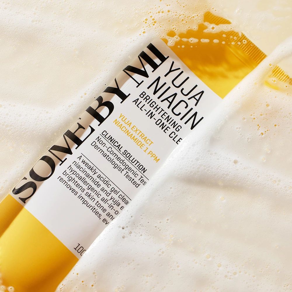 Tubo giallo con etichetta bianca, parzialmente nella schiuma di sapone. Scritta: Yuja Niacin Brightening All-in-One Cleanser.