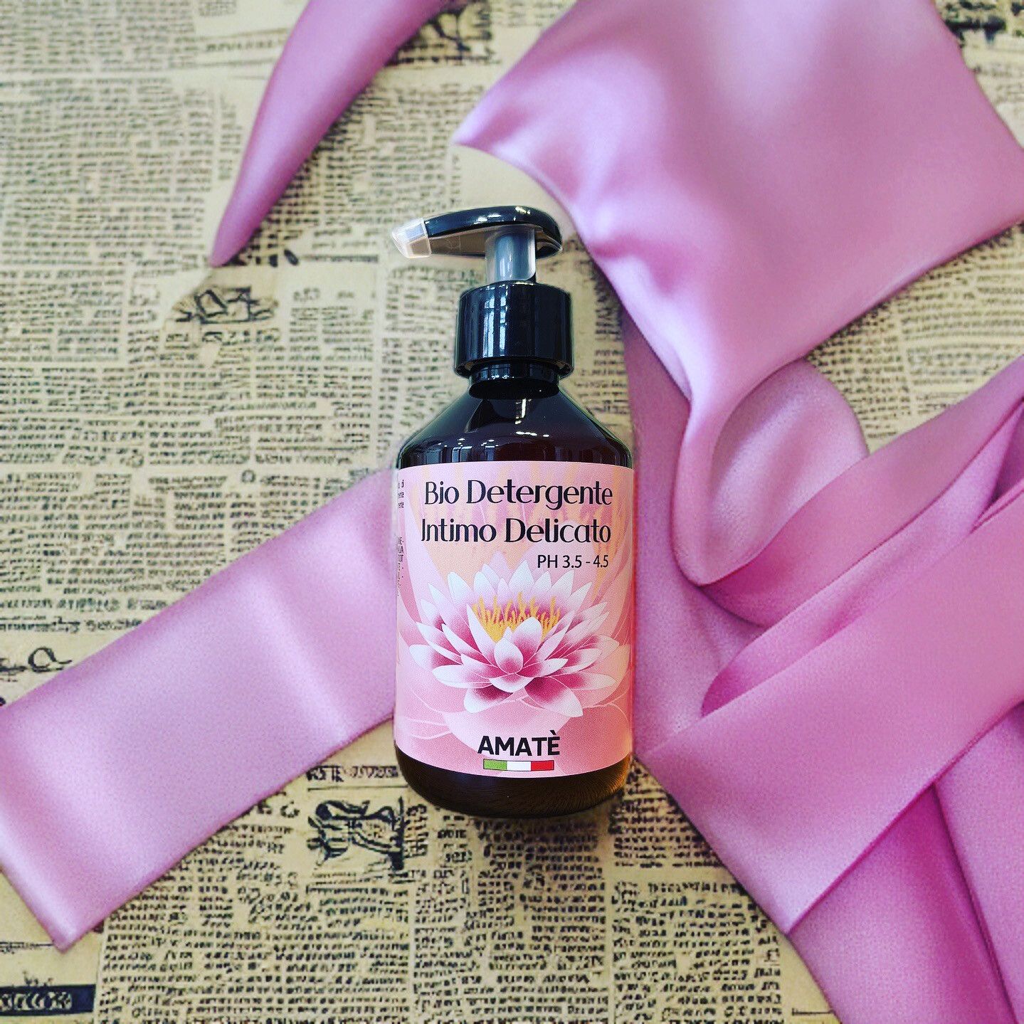 Flacone marrone con dosatore nero. Etichetta con nome del prodotto e fiore di loto. Bandiera italiana. Su tessuto rosa.